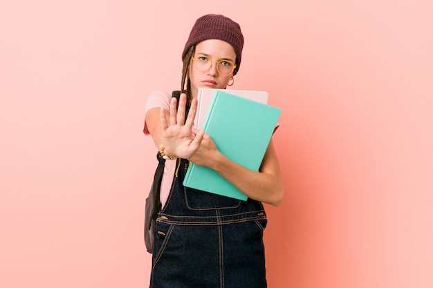 Jeune femme caucasienne tenant des cahiers debout avec la main tendue montrant le panneau d'arrêt, vous empêchant.