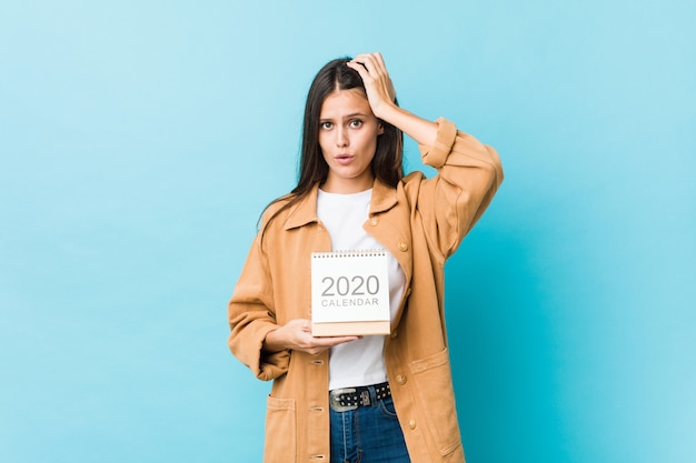 Jeune femme caucasienne tenant un calendrier des années 2020 étant choquée, elle s'est souvenue d'une réunion importante.