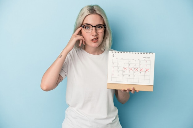 Jeune Femme Caucasienne Tenant Un Calendrier Isolé Sur Fond Bleu Montrant Un Geste De Déception Avec L'index.