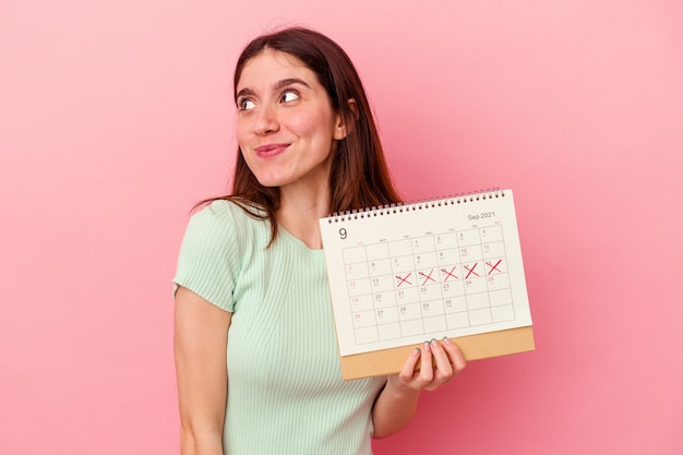 Jeune femme caucasienne tenant un calendrier isolé sur un mur rose rêvant d'atteindre des objectifs et des buts