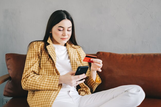 Jeune femme caucasienne tenant une carte de crédit, utilisant un smartphone et des achats en ligne.