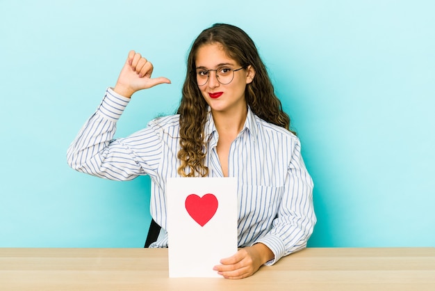 Jeune femme caucasienne tenant une carte de Saint Valentin isolée se sent fière et confiante, exemple à suivre.