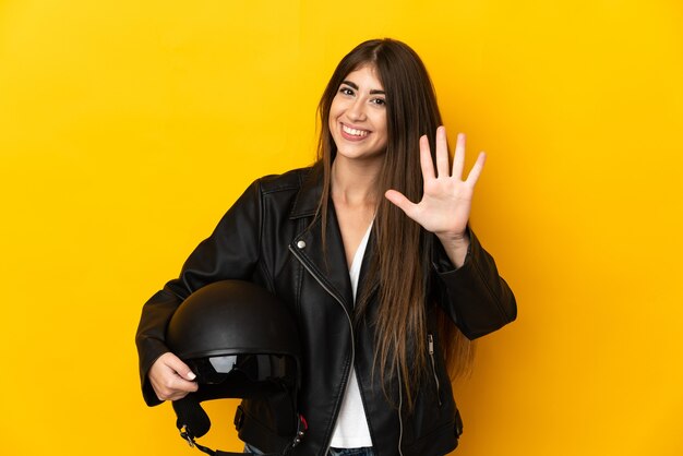 Jeune femme caucasienne tenant un casque de moto isolé sur fond jaune comptant cinq avec les doigts