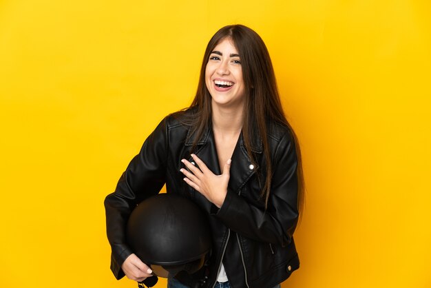 Jeune femme caucasienne tenant un casque de moto isolé sur fond jaune souriant beaucoup