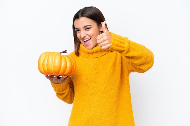 Jeune femme caucasienne tenant une citrouille isolée sur fond blanc avec les pouces vers le haut parce que quelque chose de bien s'est produit