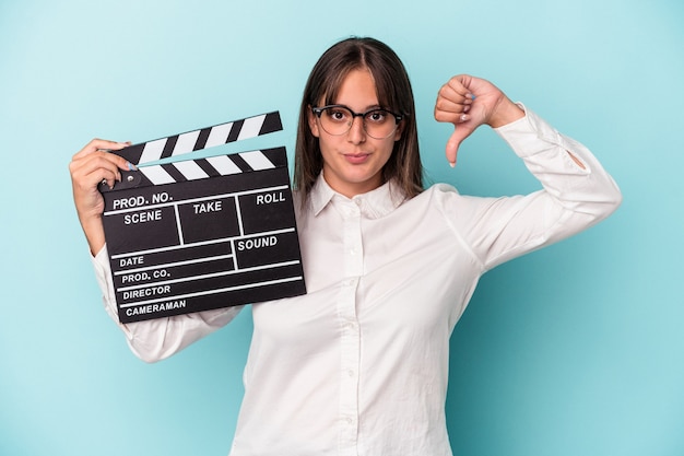 Jeune Femme Caucasienne Tenant Un Clap Isolé Sur Fond Bleu Montrant Un Geste D'aversion, Les Pouces Vers Le Bas. Notion De Désaccord.