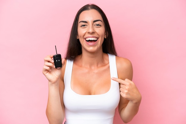 Jeune femme caucasienne tenant des clés de voiture isolées sur fond rose avec une expression faciale surprise