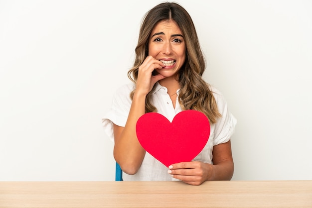 Jeune femme caucasienne tenant un coeur de Saint Valentin isolé les ongles mordants, nerveux et très anxieux.