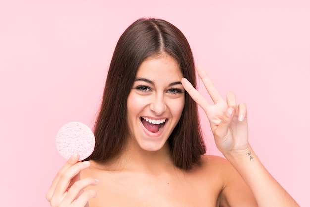 Jeune femme caucasienne tenant un disque facial isolé montrant le signe de la victoire et souriant largement.