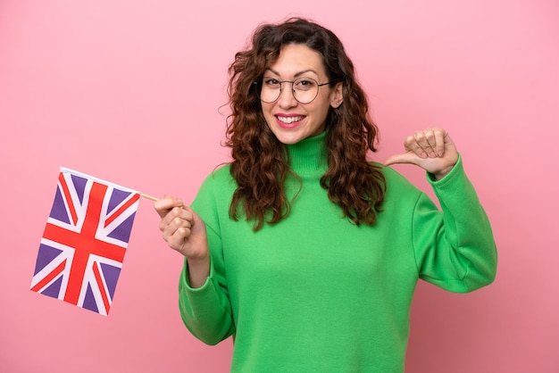 Jeune femme caucasienne tenant un drapeau anglais isolé sur fond rose fier et satisfait de soi