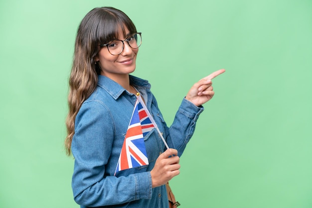 Jeune femme caucasienne tenant un drapeau du Royaume-Uni sur fond isolé pointant le doigt sur le côté