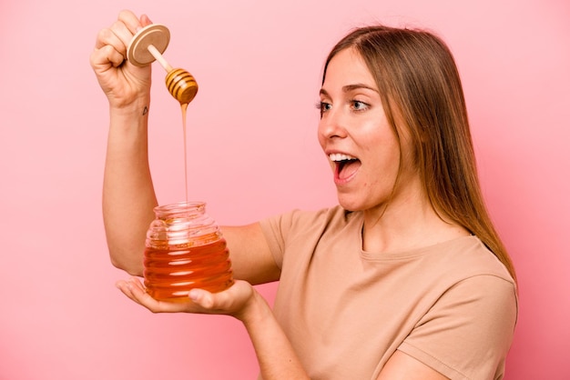 Jeune femme caucasienne tenant du miel isolé sur fond rose