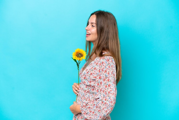 Jeune femme caucasienne tenant du tournesol isolé sur fond bleu en riant en position latérale