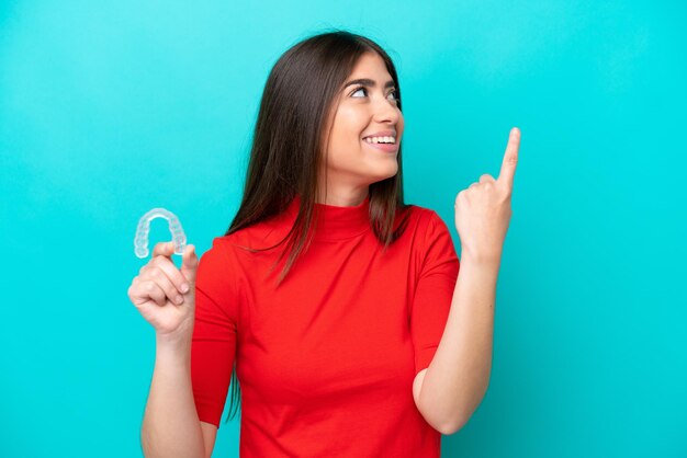 Jeune femme caucasienne tenant un envisageant isolé sur fond bleu dans l'intention de réaliser la solution tout en levant un doigt