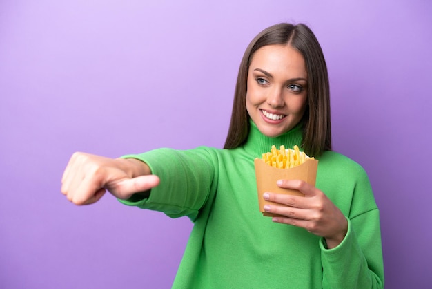 Jeune femme caucasienne tenant des frites frites sur fond violet donnant un geste du pouce levé