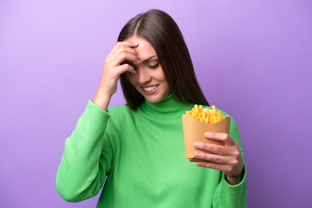 Jeune femme caucasienne tenant des frites frites sur fond violet en riant