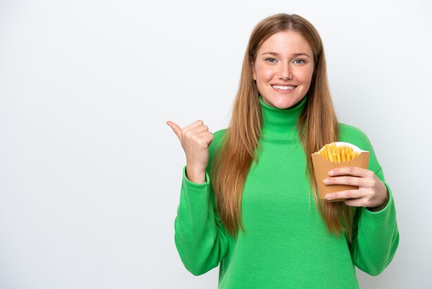 Jeune femme caucasienne tenant des frites frites isolées sur fond blanc pointant vers le côté pour présenter un produit