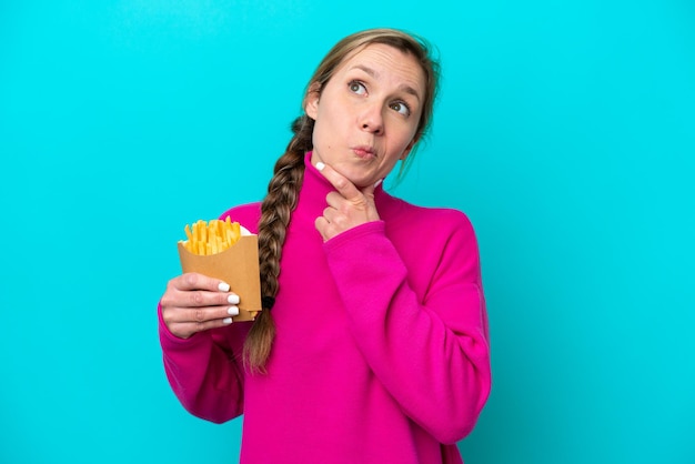 Jeune femme caucasienne tenant des frites frites isolées sur fond bleu et levant les yeux