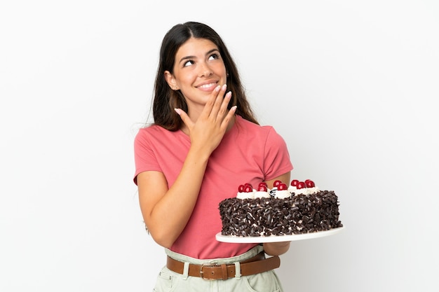 Jeune femme caucasienne tenant un gâteau d'anniversaire isolé sur fond blanc en levant tout en souriant