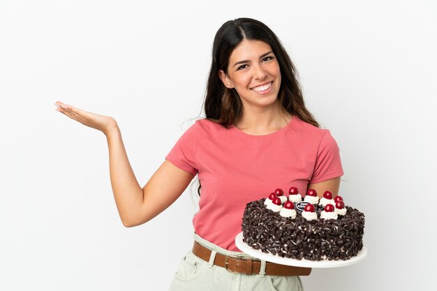 Jeune femme caucasienne tenant un gâteau d'anniversaire isolé sur fond blanc tendant les mains sur le côté pour inviter à venir