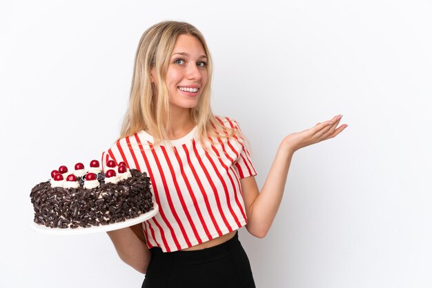 Jeune femme caucasienne tenant un gâteau d'anniversaire isolé sur fond blanc tendant les mains sur le côté pour inviter à venir