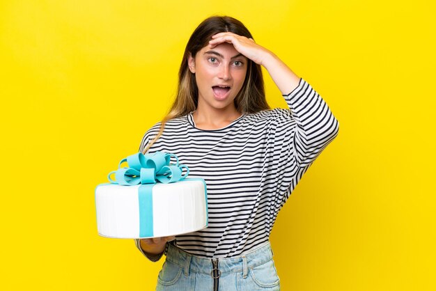 Photo jeune femme caucasienne tenant un gâteau d'anniversaire isolé sur fond jaune faisant un geste de surprise tout en regardant sur le côté