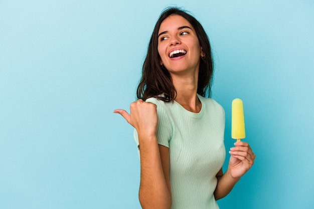 Jeune femme caucasienne tenant une glace isolée sur fond bleu Jeune femme caucasienne tenant une glace isolée sur fond bleu points avec le pouce loin, riant et insouciant.