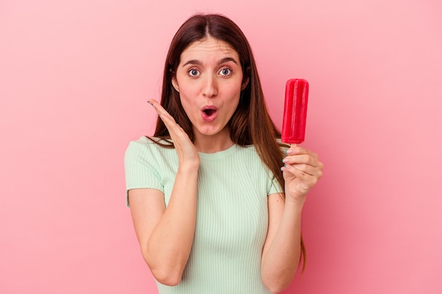 Jeune femme caucasienne tenant une glace isolée sur fond bleu surpris et choqué.