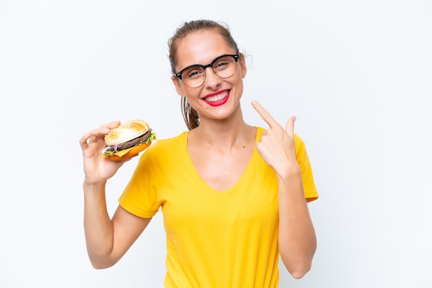 Jeune femme caucasienne tenant un hamburger isolé sur fond blanc donnant un geste du pouce levé