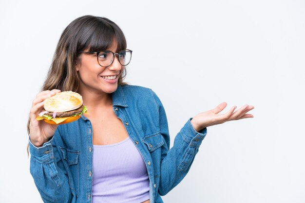 Jeune femme caucasienne tenant un hamburger isolé sur fond blanc avec une expression faciale surprise