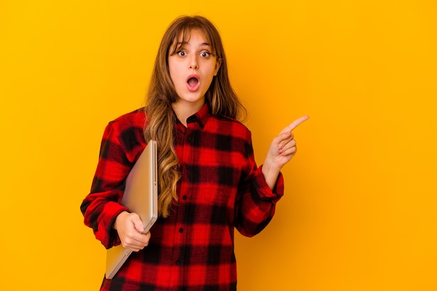 Jeune femme caucasienne tenant un ordinateur portable isolé pointant vers le côté