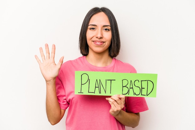 Jeune femme caucasienne tenant une pancarte à base de plantes isolée sur fond blanc souriant joyeux montrant le numéro cinq avec les doigts