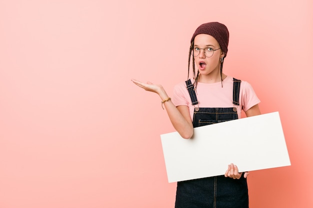 Jeune femme caucasienne tenant une pancarte impressionné tenant l'espace copie sur la paume.