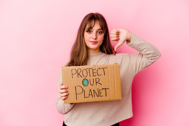 Jeune femme caucasienne tenant une pancarte Protégez notre planète isolée montrant un geste d'aversion, les pouces vers le bas. Notion de désaccord.