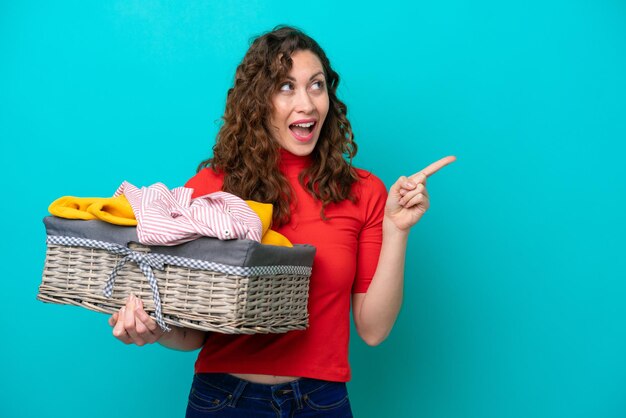 Jeune femme caucasienne tenant un panier à vêtements isolé sur fond bleu dans l'intention de réaliser la solution tout en levant un doigt