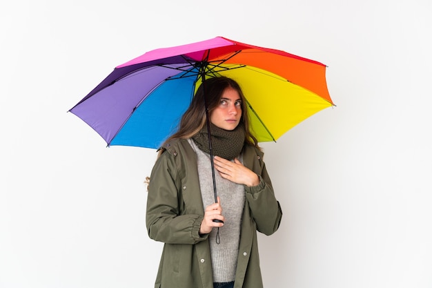 Jeune femme caucasienne tenant un parapluie isolé sur fond blanc ayant des doutes et de la pensée