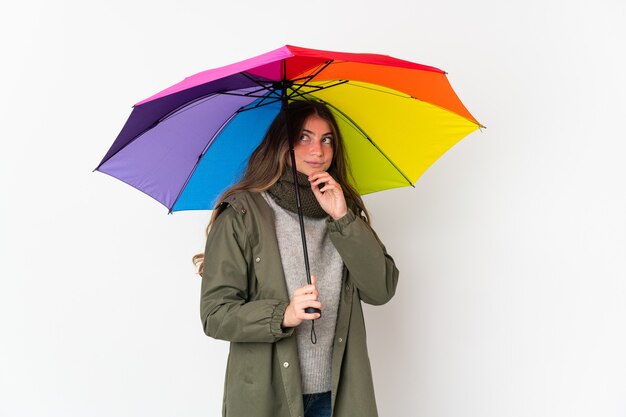 Jeune femme caucasienne tenant un parapluie isolé sur un mur blanc et levant