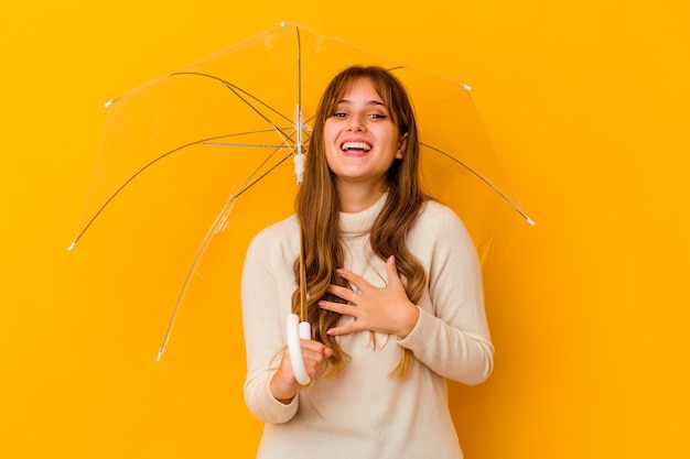 Jeune femme caucasienne tenant un parapluie isolé rit bruyamment en gardant la main sur la poitrine.