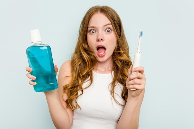 Jeune femme caucasienne tenant un rince-bouche et une brosse à dents isolés sur fond bleu