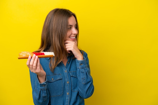 Jeune femme caucasienne tenant sashimi isolé sur fond jaune pensant une idée et regardant de côté