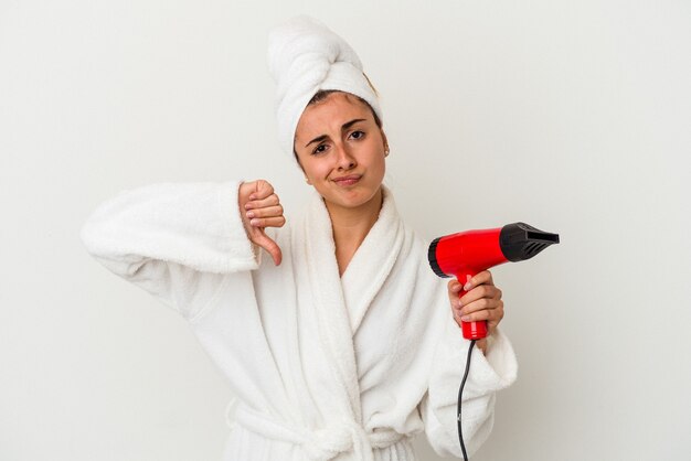 Jeune femme caucasienne tenant un sèche-cheveux isolé sur blanc montrant un geste de dégoût, les pouces vers le bas. Concept de désaccord.