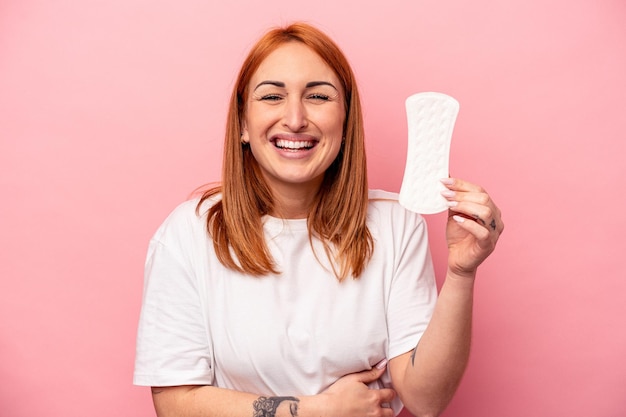 Photo jeune femme caucasienne tenant une serviette hygiénique isolée sur fond rose en riant et en s'amusant