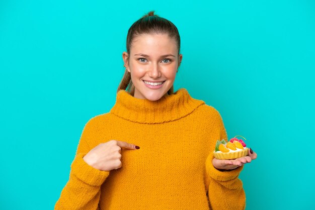 Photo jeune femme caucasienne tenant une tartelette isolée sur fond bleu avec une expression faciale surprise