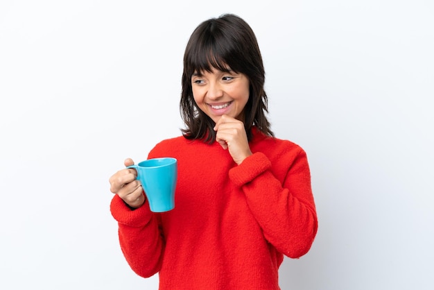 Jeune femme caucasienne tenant une tasse de café isolé sur fond blanc regardant sur le côté et souriant