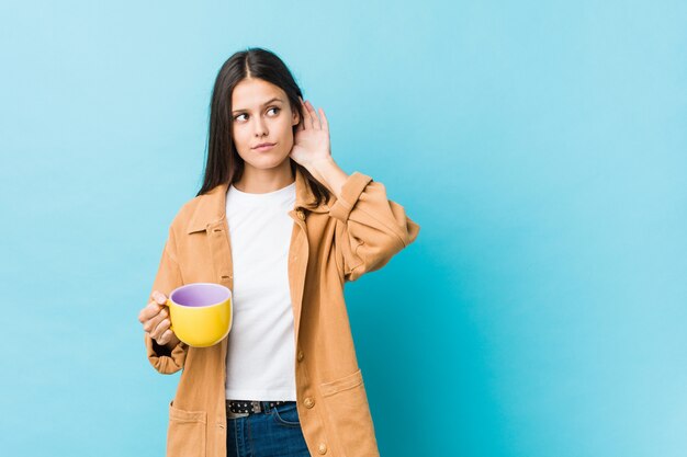 Jeune Femme Caucasienne Tenant Une Tasse De Café En Train D'écouter Un Potin.