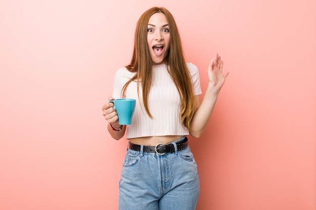 Jeune femme caucasienne tenant une tasse célébrant une victoire ou un succès