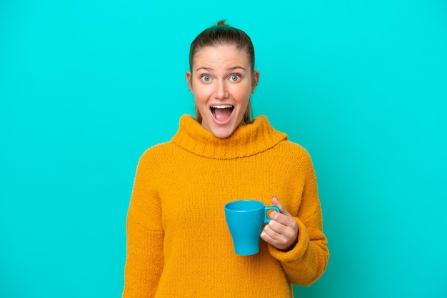 Jeune femme caucasienne tenant une tasse isolée sur fond bleu avec une expression faciale surprise et choquée