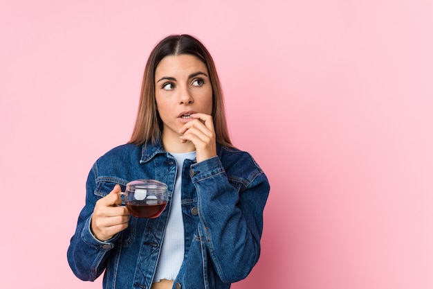 Jeune femme caucasienne tenant une tasse de thé détendue en pensant à quelque chose en regardant un espace copie.