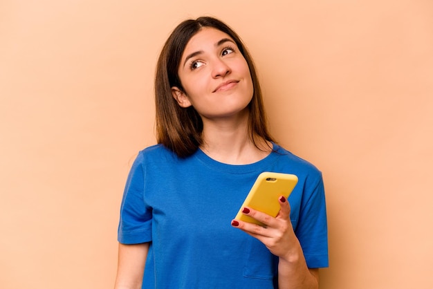 Jeune femme caucasienne tenant un téléphone portable isolé sur fond beige