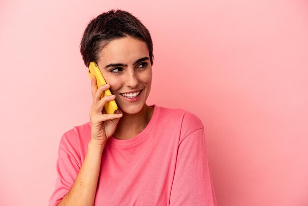 Jeune femme caucasienne tenant un téléphone portable isolé sur fond rose